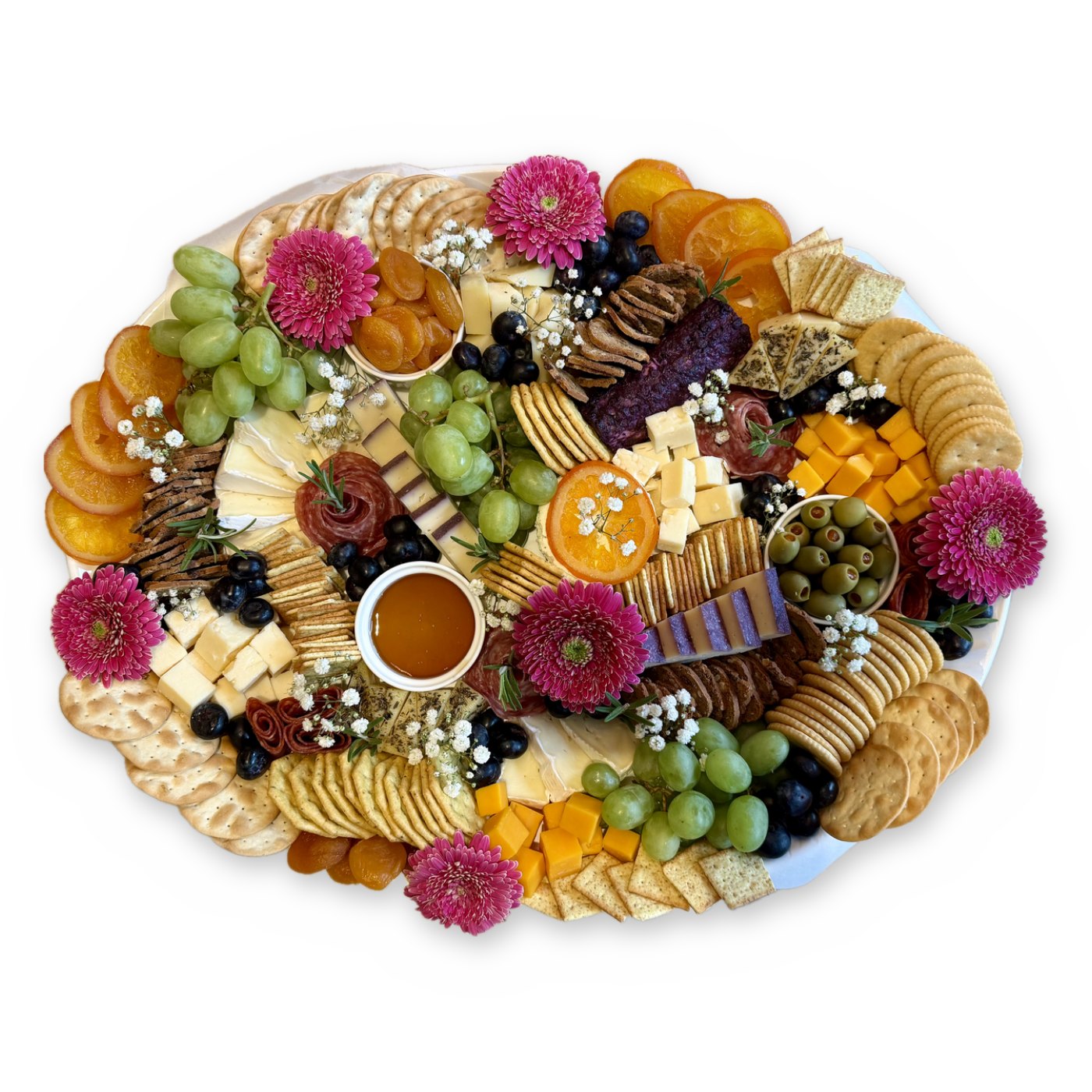 An oval white platter of cheeses, cured meats, grapes, dried oranges, crackers, honey and pink flowers