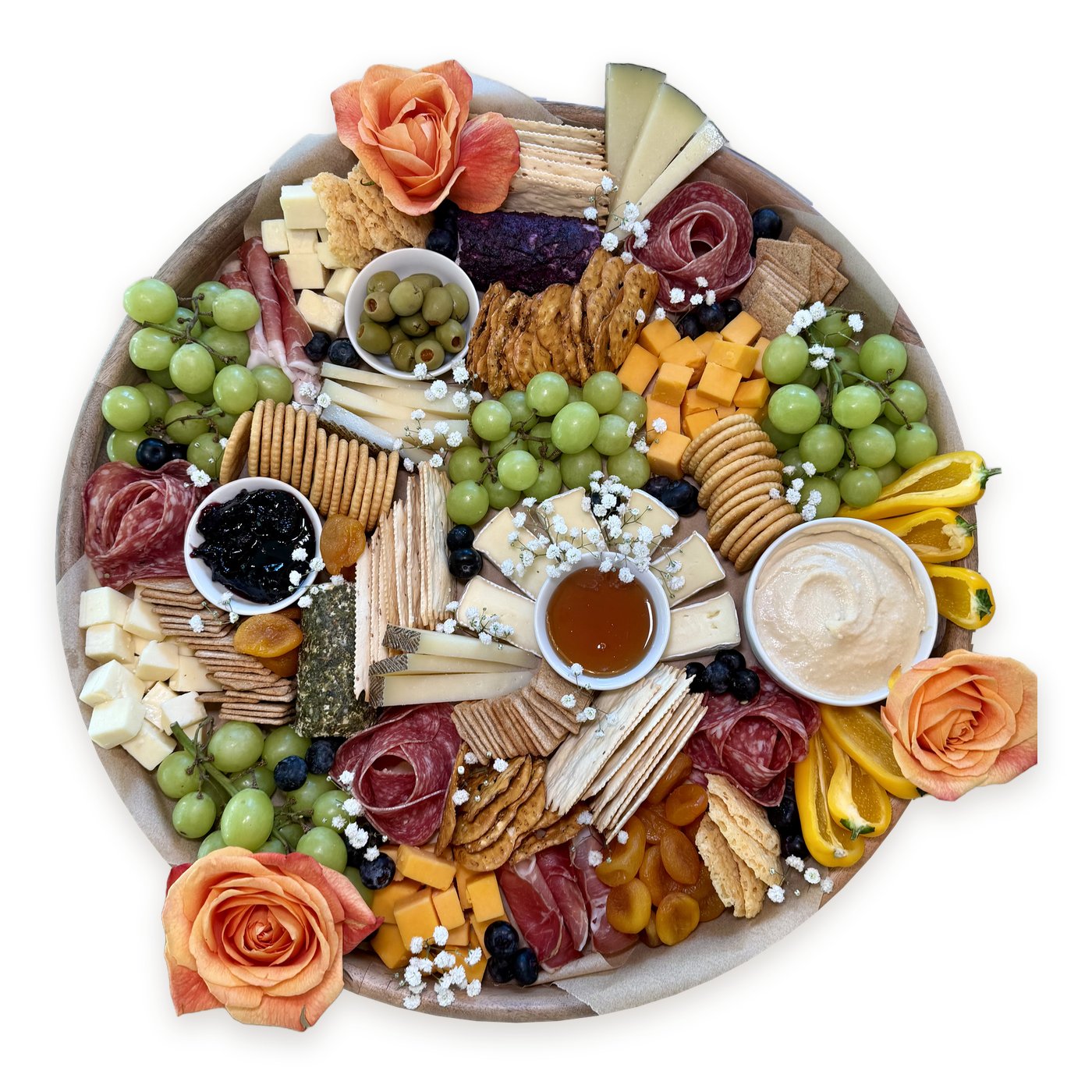 Round charcuterie board with peach roses, salami roses, cheeses, green grapes, honey, hummus and mini peppers