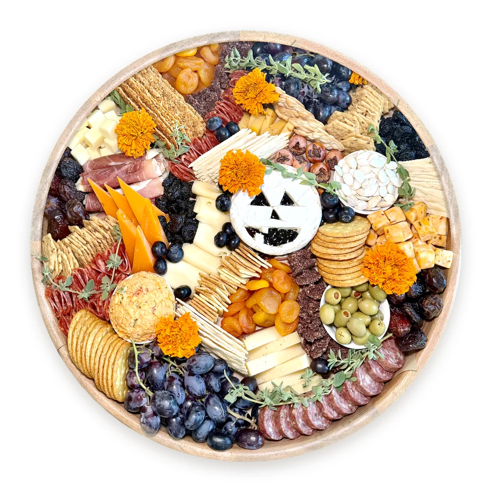 A Halloween charcuterie board with a jack-o'-lantern brie, marigolds, grapes, cheeses and crackers
